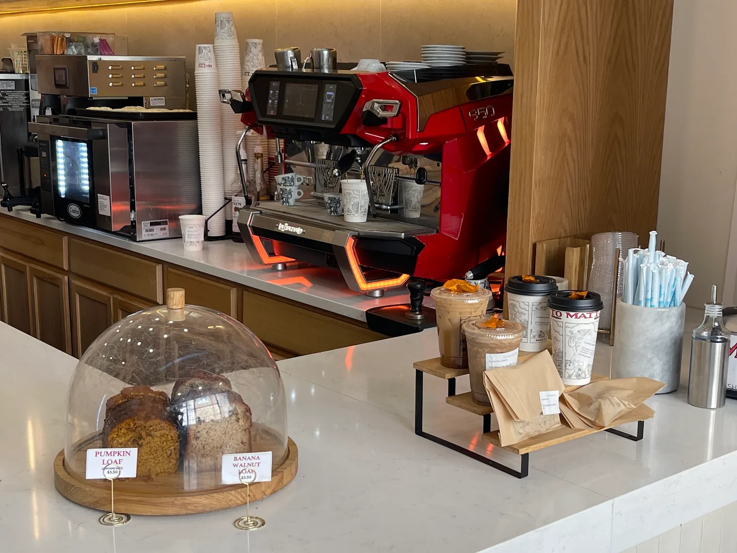 A red espresso machine, coffee cups, and pastries at the Matto counter